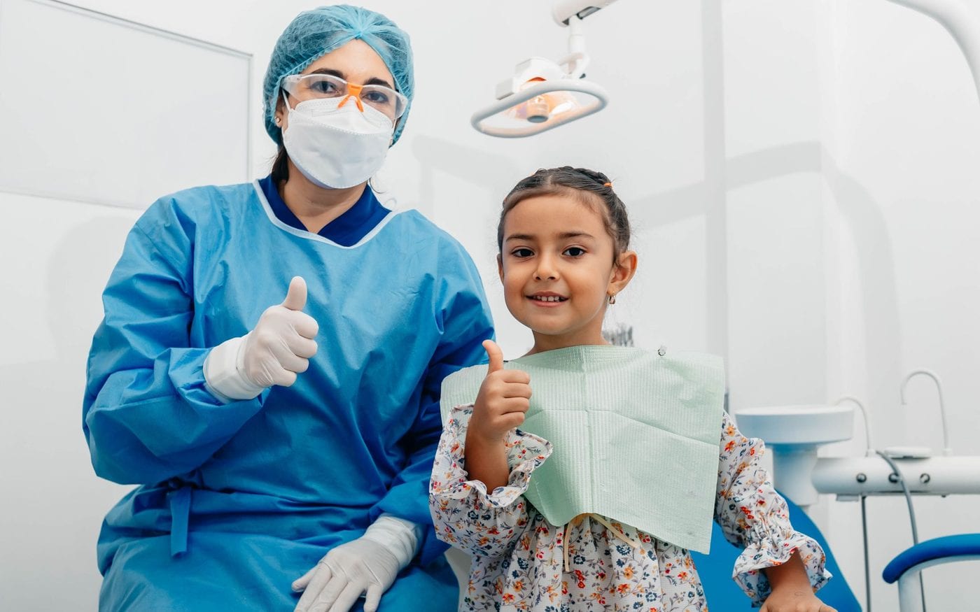 Young girl and her dentist giving a thumbs up in the clinic