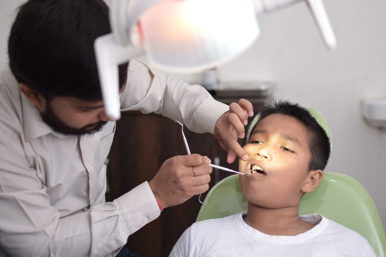 Dentist checking a young boy's teeth while he lies back in the chair