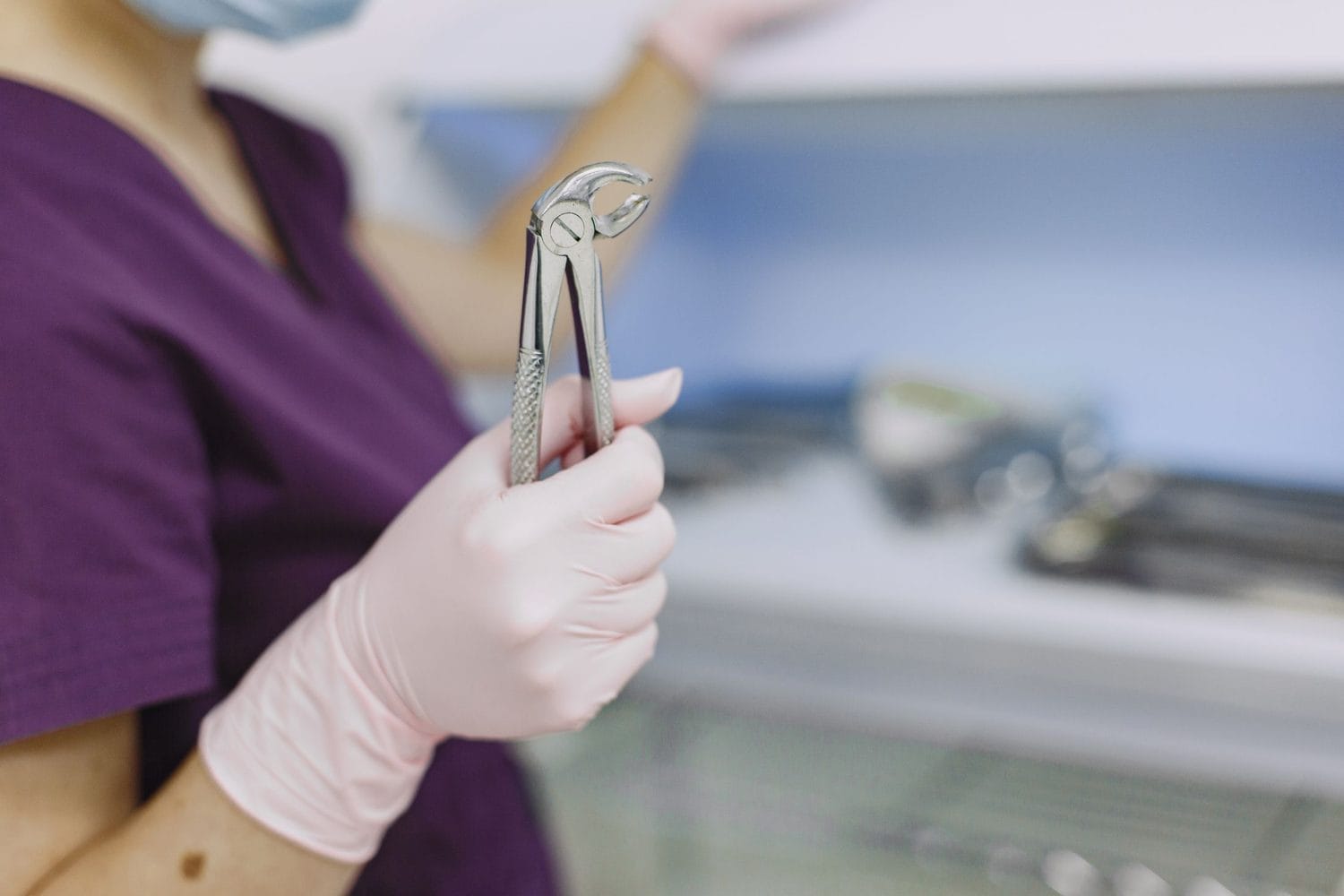 Gloved hand holding extraction forceps beside a laid out surgical tray
